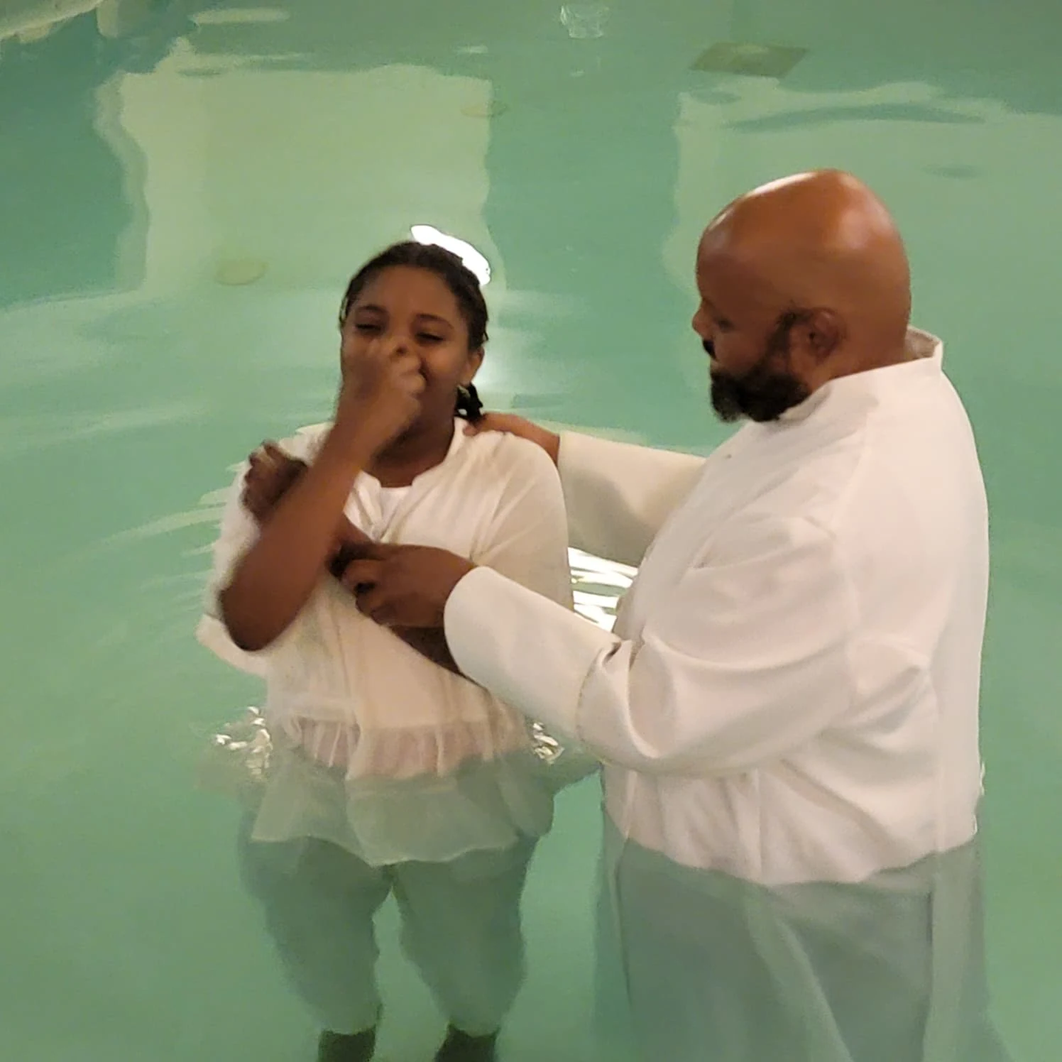 A minister supporting a young person during a baptism.