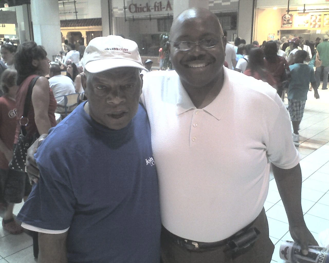Two men smiling together at a busy indoor gathering.