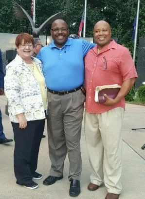 Three people standing together outdoors beside a memorial.