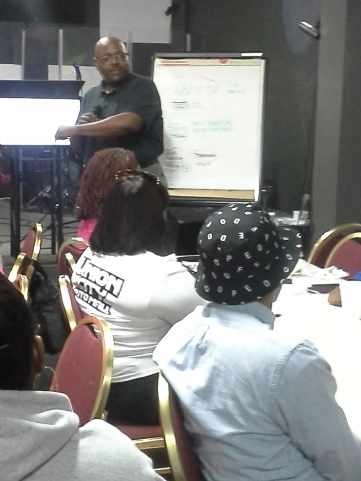 A presenter speaking into a microphone beside a flip chart during a workshop.