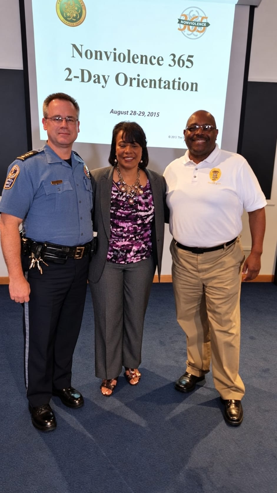 Three participants standing together in front of a Nonviolence 365 two-day orientation presentation dated August 28–29, 2015.